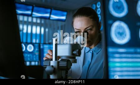 Female Medical Research Scientist Looking Through the Microscope Types Acquired Data in the Computer. Laboratory. In the Laboratory with Multiple Stock Photo