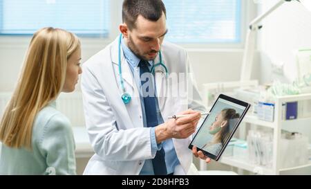 Plastic Cosmetic Surgeon Consults Woman about Facial Lift Surgery, He Draws Arrows on Digital Tablet Computer Screen, Showing Types of Facelift Stock Photo