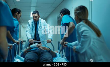 Emergency Department Doctors, Nurses and Surgeons Move Seriously Injured Patient Lying on a Gurney Through Hospital Corridors. Medical Staff in a Stock Photo