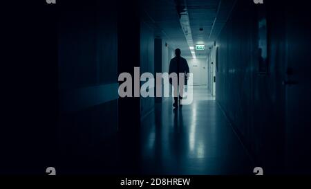 Medical Doctor Silhouette Walks in Dark Part of the Hospital Corridor. Stock Photo