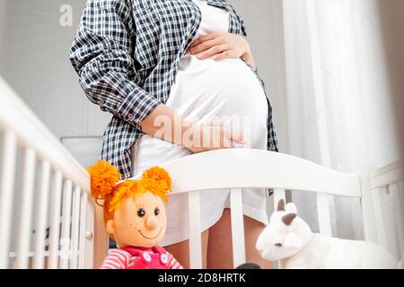 A young pregnant woman hugs her belly. View from below, from the baby's cradle. Concept of pregnancy and happy motherhood. Close up. Stock Photo