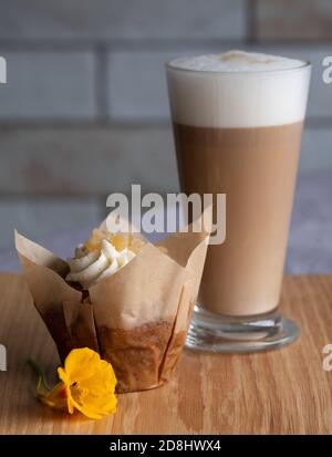 Glass of vegan dairy free milk latte coffee, with vegan cupcake in foreground. Served on wooden platter and decorated with orange nasturtium flower. Stock Photo