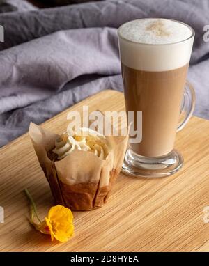 Glass of vegan dairy free milk latte coffee, with vegan cupcake in foreground. Served on wooden platter and decorated with orange nasturtium flower. Stock Photo