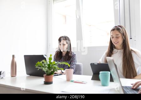 Cheerful female colleagues using laptop and table to make video calls in office Stock Photo