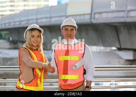 Female industrial engineer wearing a white helmet while standing in a construction site with businessman talking on working plan, Engineer and archite Stock Photo