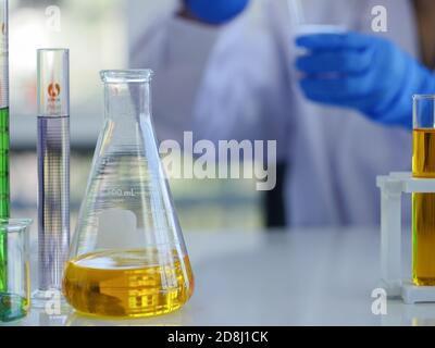 Closeup laboratory glassware such as conical flask and measuring cylinder with scientific research on the table in front of scientists in the lab. Stock Photo