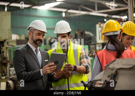 Male Industrial Engineers Talk with Factory Worker . They Work at the Heavy Industry Manufacturing Facility. Stock Photo