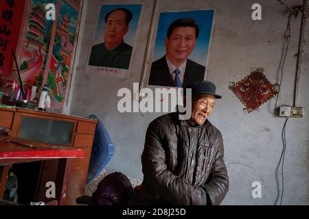 An elderly man stands in front of the portraits of Xi Jinping and Mao Zedong seen pasted at his home.Many people in China are very respectful to Xi Jinping and Mao Zedong. Especially in the countryside, people are willing to post pictures of Xi Jinping and Mao Zedong at home as a respect to the country's leaders. Stock Photo