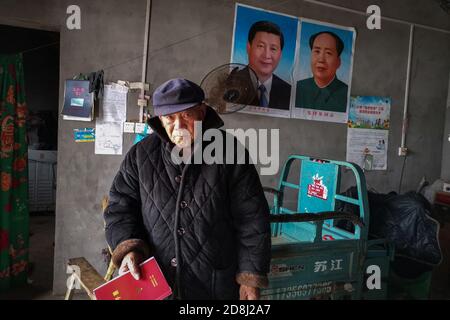 An elderly man stands in front of the portraits of Xi Jinping and Mao Zedong seen pasted at his home.Many people in China are very respectful to Xi Jinping and Mao Zedong. Especially in the countryside, people are willing to post pictures of Xi Jinping and Mao Zedong at home as a respect to the country's leaders. Stock Photo