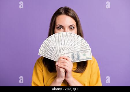 Photo of lovely young lady hold fan cash close face look camera wear yellow shirt isolated purple color background Stock Photo