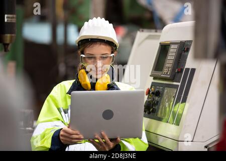 Female technician worker in uniform working on laptop with machine in manufacturing. Stock Photo