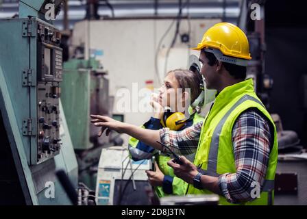 Men and female workers in factory operating machine in workshop floor. Stock Photo