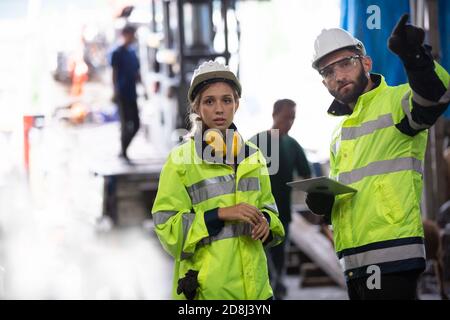 Men and female workers in factory operating machine in workshop floor. Stock Photo