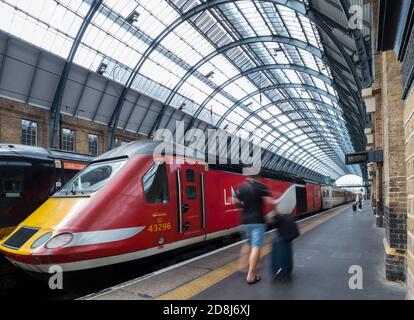 London North Eastern Railway train on the platform at Kings Cross, London with passengers rushing by with luggage Stock Photo
