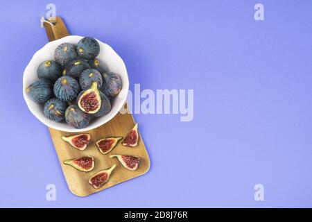 Bowl with whole and cut ripe figs on a blue background. Copy space. Stock Photo