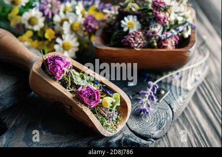 medicinal herbal tea with chamomile flowers and a bouquet of wild flowers in a wooden scoop on a rustic wooden background. Rustic still life Stock Photo