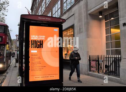 A woman with a face mask walks past a Local Covid Alert Level High sign in Central London. The UK government has introduced a new three-tier system with restrictions increasing depending on the levels in each area. Stock Photo