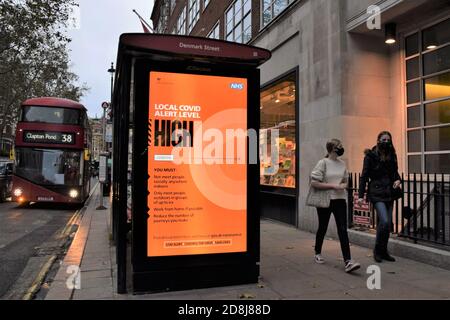 People with face masks walk past a Local Covid Alert Level High sign in Central London. The UK government has introduced a new three-tier system with restrictions increasing depending on the levels in each area. Stock Photo