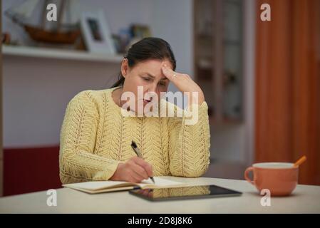 Worried senior woman in yellow sweater writing Stock Photo