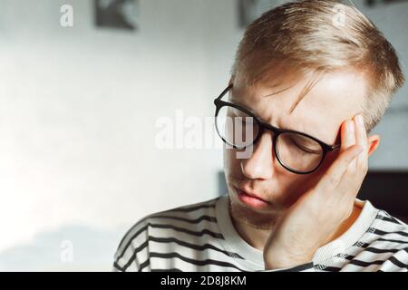 Unhappy stressed young caucasian man suffering from headache. Upset exhausted guy feeling frustrated depressed tired touching forehead suffer from mig Stock Photo