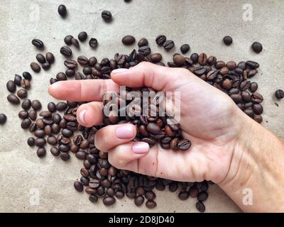 Fresh roasted coffee beans pouring out of folded palms on cardboard brown background. Fragrant coffee beans concept Stock Photo