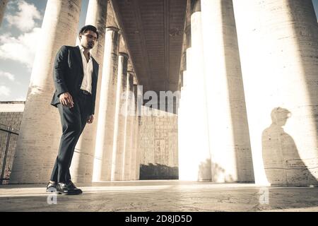 Elegant dressed man with down look walking outdoors near ancient columns. Stock Photo
