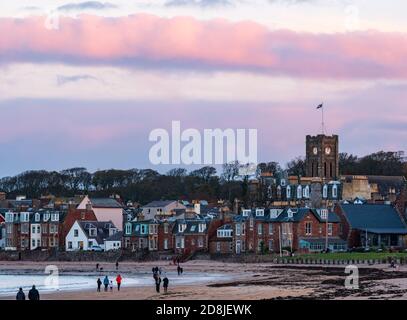 North Berwick, East Lothian, Scotland, United Kingdom, 30th October 2020. UK Weather: sunset with a colourful pink sky over the skyline of the seaside town from West Beach with people walking on the beach in West Bay Stock Photo