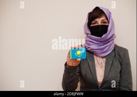 Portrait of young muslim woman wearing formal wear, protect face mask and hijab head scarf, hold Kazakhstan flag card against isolated background. Cor Stock Photo