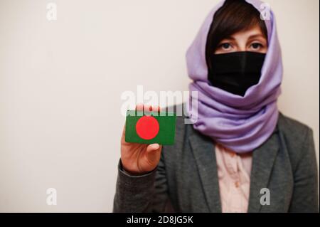 Portrait of young muslim woman wearing formal wear, protect face mask and hijab head scarf, hold Bangladesh flag card against isolated background. Cor Stock Photo