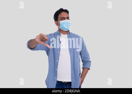 Indian Man Wearing Medical Mask Showing Thumb Down Isolated. Man In Blue Shirt with Medical Mask. Health, Virus, Medical Concept Stock Photo