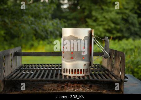 Close up image of a charcoal chimney starter placed on top of an outdoor grill in a picnic location. This metal tool is a convenient way to get charco Stock Photo