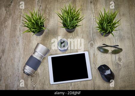 photo lens, sunglasses, mouse and tablet on wooden table with plants Stock Photo