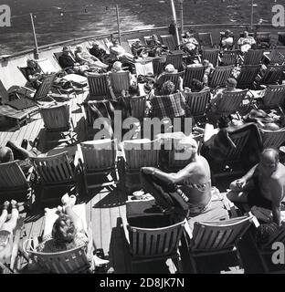 1960s, historical, passengers sitting, relaxing on deckchairs outside on the cruise ship, Sagafjord, in the era when cruising was a simpler affair and a rest in the fresh air was the order of the day. Stock Photo