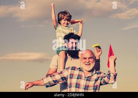 Generation of people and stages of growing up. Child pilot aviator with paper airplane dreams of traveling. Young boy with father and grandfather Stock Photo