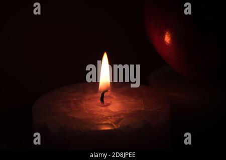 burning candle with flame reflecting on a red fruit Stock Photo