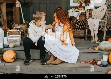 children a boy and a girl with their poodle dog in protective masks on the porch of the backyard decorated with pumpkins in autumn, the concept of the Stock Photo