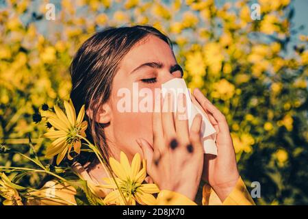 Young girl sneezing and holding paper tissue in one hand and flower bouquet in other. Young woman got nose allergy, flu sneezing nose. Young woman is Stock Photo