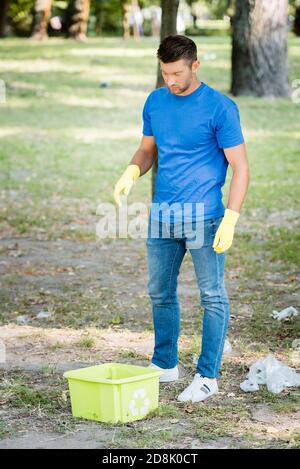 man in rubber gloves standing near container with recycling sign Stock Photo