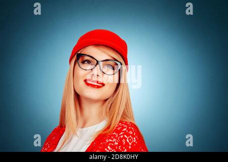 Pretty cool woman in red cap hat looking up, having fun wearing red lace jacket and white formal shirt isolated on dark blue background with copy spac Stock Photo