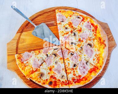 Pizza cut into pieces on a wooden tray with a metal spatula Stock Photo
