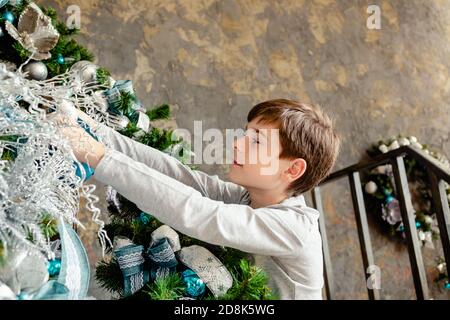 Portrait of happy boy decorating Christmas tree at living room for Christmas. Merry Christmas and Happy Holidays concept. Stock Photo