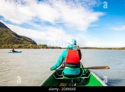 Young woman kayaking in the sea at sunny day from the back in coat Stock Photo