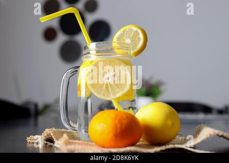 Lemonade drink in a glass jar with sliced lemon slices and a drinking tube on a decorated wooden desk with lemon and orange fruits. Healthy drink conc Stock Photo