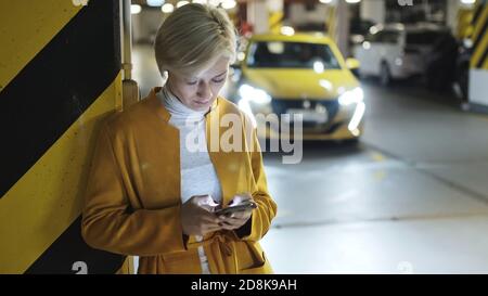 Young fashionable blond caucasian woman using smartphone in the underground parking garage. High quality photo Stock Photo