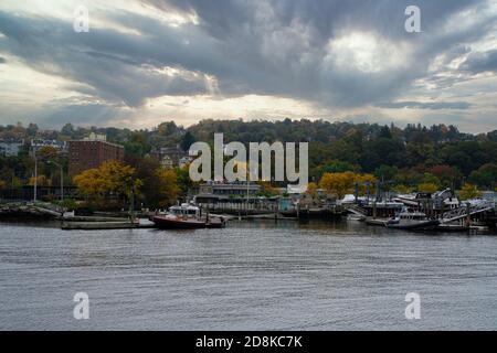 A view of a vast lake or river with several boats parked next to its coast with a dense forest visible in the distance under the cloudy autumn sky Stock Photo