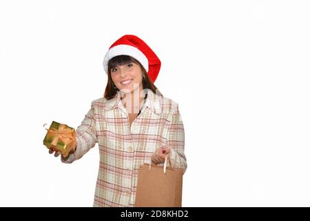 Young beautiful woman with a Santa hat smiling and offering a golden wrapped gift at the camera on a light background. Christmas and gifts concept. Stock Photo