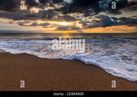 The Sun is Setting on the Ocean Horizon as Sun Rays Burst Through The Clouds Stock Photo