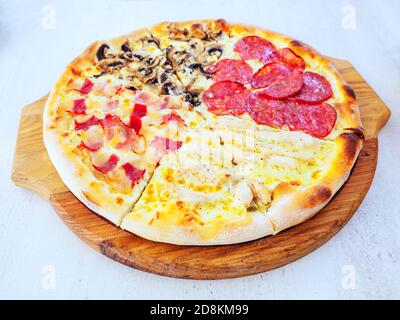 Round pizza with four different fillings cut into pieces on a wooden tray. Stock Photo