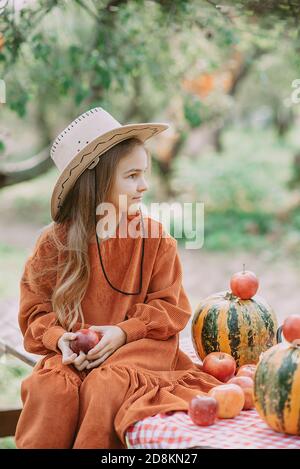 Autumn portrait of child on pumpkin patch on cold autumn day with a lot of pumpkins and apples for halloween or thanksgiving. Child picking pumpkin at Stock Photo