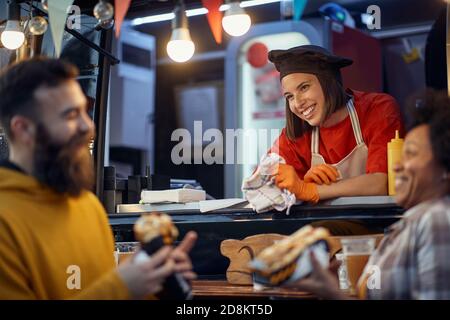 friends socializing with employee in fast food service, eating sandwiches, talking, laughing, smiling Stock Photo